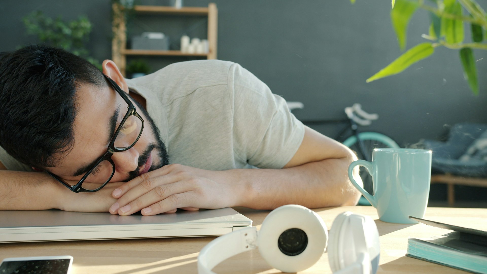 Man sleeping at desk with headphones and coffee.